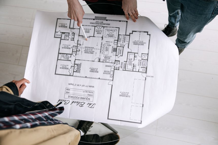 Twee mensen buigen zich over een plattegrond op tafel, een van hen wijst een ruimte aan.